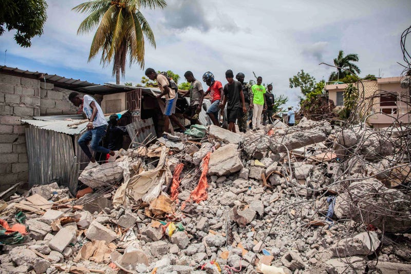 People walk over a pile of rubble from a collapsed building after a 7.2-magnitude earthquake struck Haiti on August 16, 2021 in Les Cayes, Haiti.