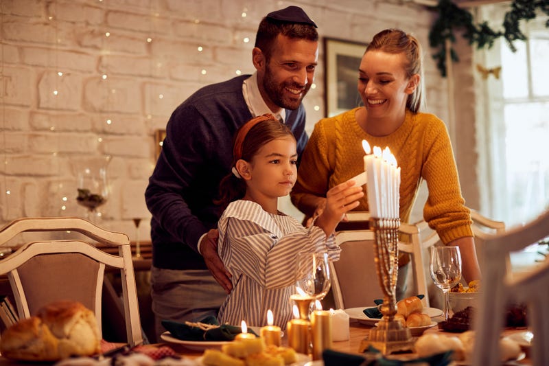 Happy Jewish family lightning the menorah before a meal at dining table