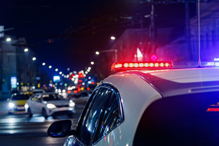 A police car at a busy intersection at night with the emergency lights flashing.