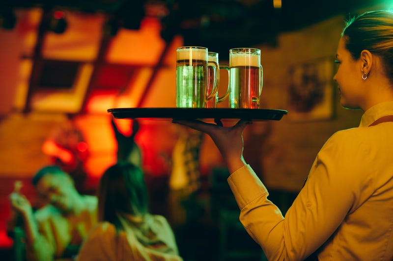 waitress carrying tray with beer glasses while serving customers in a pub