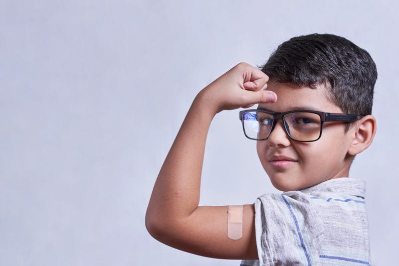 Portrait of happy healthy young kid showing bandage plaster on arm shoulder after getting vaccination