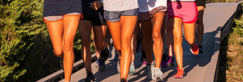 Legs of female runners in shorts running in the sunshine on a boardwalk at the beach