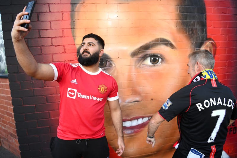 Fans of Manchester United pose for a photograph next to a mural of Cristiano Ronaldo of Manchester United which is located outside the stadium prior to the UEFA Champions League group F match between Manchester United and Villarreal CF at Old Trafford on September 29, 2021 in Manchester, England.