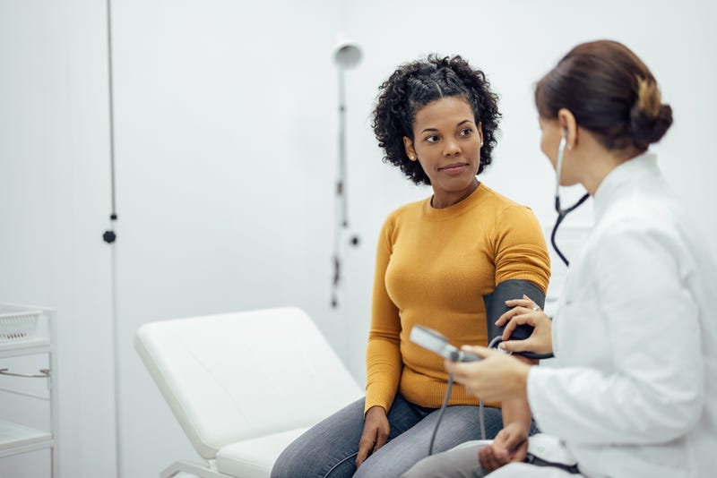 A doctor measures a Black woman's blood pressure.