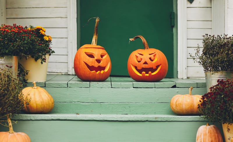 House entrance with halloween pumpkin decoration on wooden stairs, two jack o lanterns with spooky faces on porch of apartment building during all hallows eve