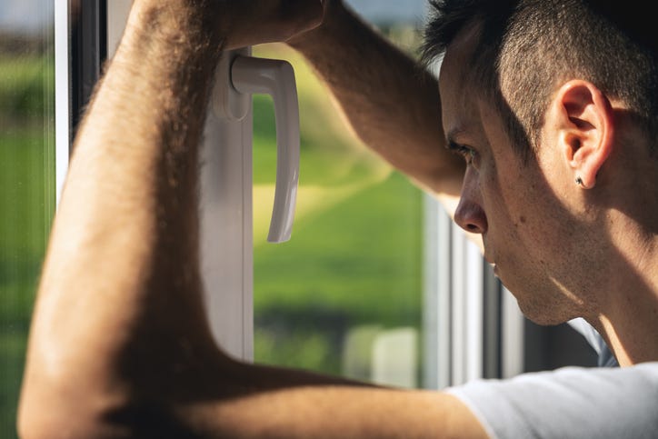 Sad, desperate young man looks out of window alone, symbol of hopelessness, fear, quarantine, sickness and mental health