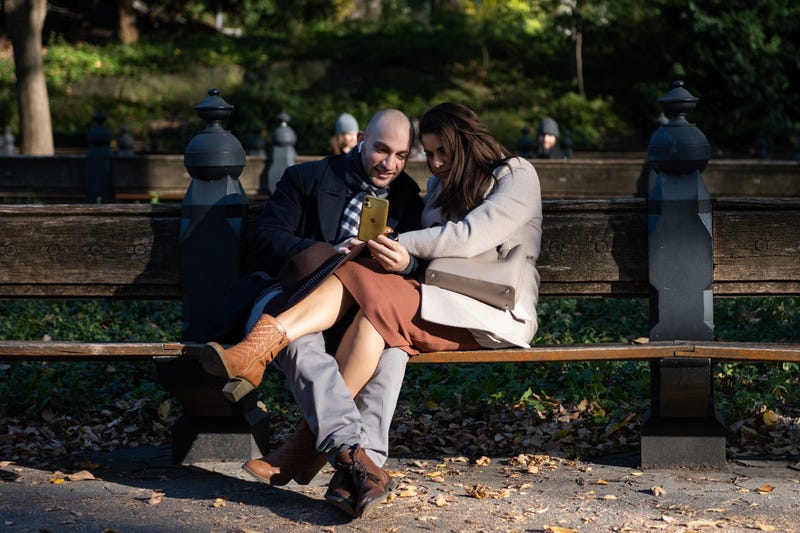 A couple looks at an iPhone while sitting with legs intertwined in Central Park on November 06, 2021 in New York City. 