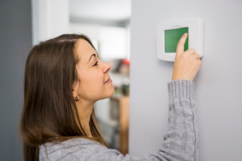 FILE: A woman adjusts a thermostat.