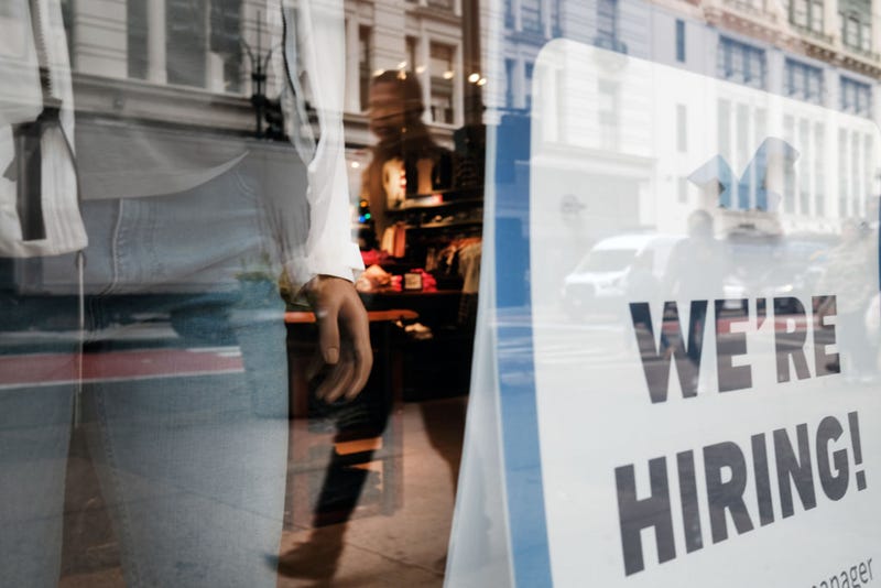 : People walk by a hiring sign in a window along a main shopping street in Manhattan on November 17, 2021 in New York City.