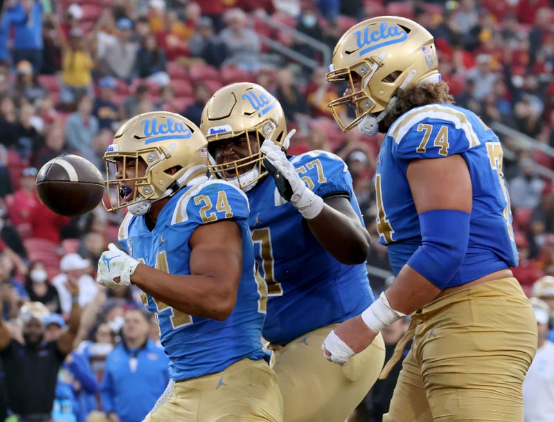 Zach Charbonnet #24 of the UCLA Bruins celebrates his touchdown run with Yutaka Mahe #67 and Sean Rhyan #74, to take a 48-26 lead over the USC Trojans, at Los Angeles Memorial Coliseum on November 20, 2021 in Los Angeles, California.
