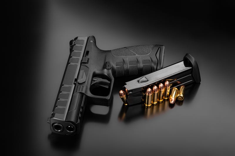 Black modern gun and ammunition for it on a dark reflective surface.