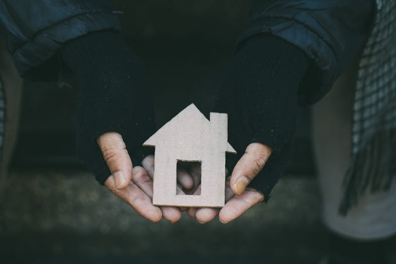 Homeless person holding a cut out of a home.