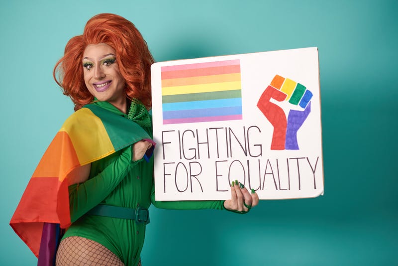 Optimistic transgender person with LGBT flag looking at camera with smile and showing placard with Fighting For Equality inscription against blue background