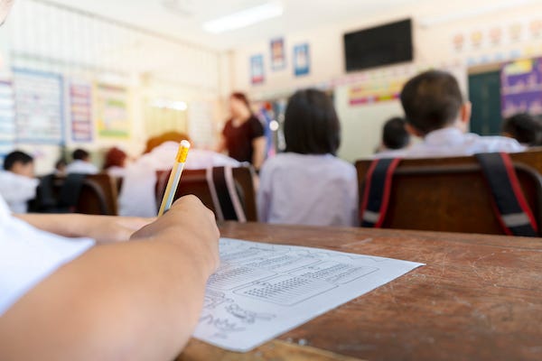 Student holding a pencil listening to a teacher in a classroom