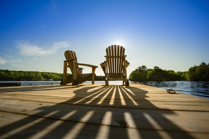  Sunrise on two empty Adirondack chairs sitting on a dock on a lake in Muskoka, Ontario Canada. 