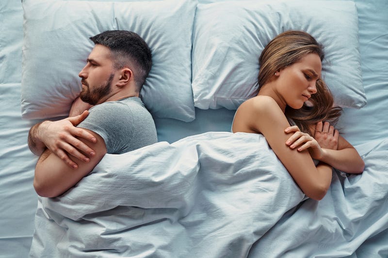 Young beautiful couple lying in bed turned back to back, arms crossed in anger and resentment. Relationship problems.Top view.