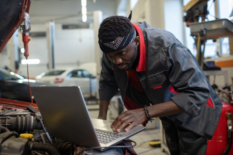 Young African repairman consulting websites while checking and repairing engine