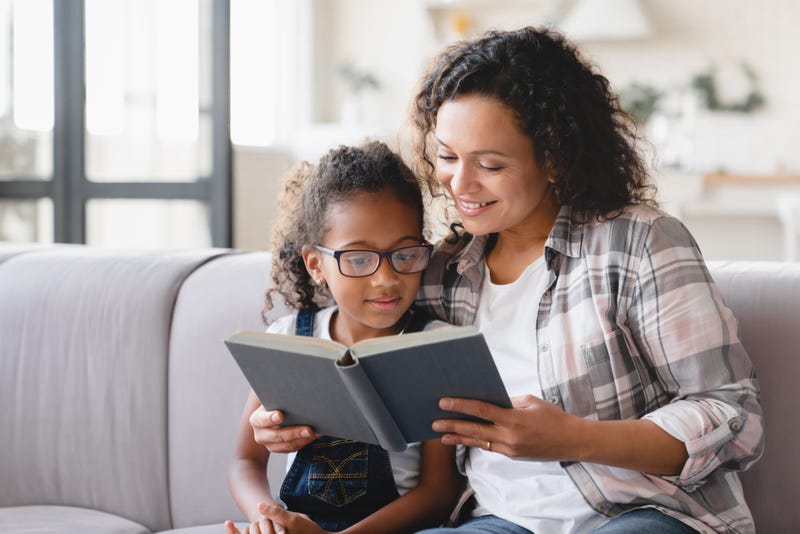 Mom reading fairy tales book novel with daughter girl, learning together, helping assisting with homework for school.