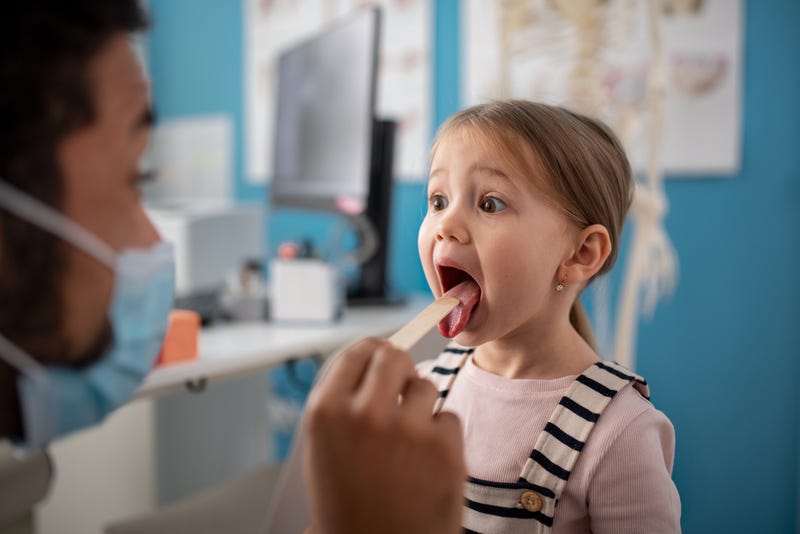 A young male doctor checking little girl's throat in his office.