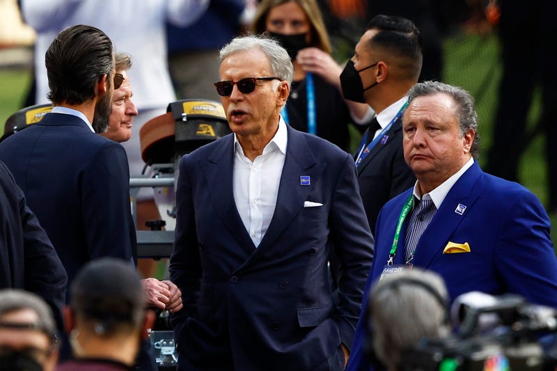 stan kroenke wears sunglasses and a suit surrounded by people at a football game