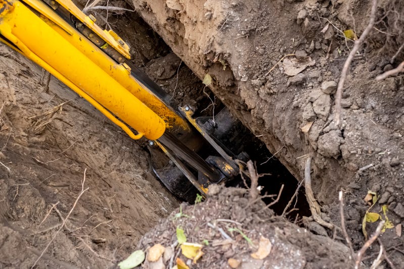 An excavator with a long boom is digging a sewer well during construction of a septic tank.