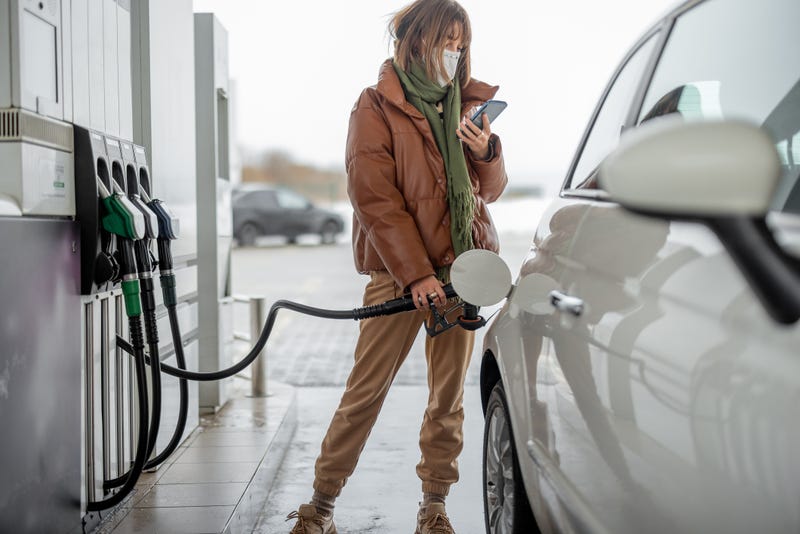 Woman in face mask refueling car with a gasoline using smart phone