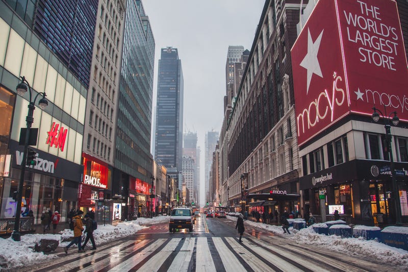 An NYC midtown street. Tourists cross the iconic intersection of 34th Street & 6th Ave carefully choosing their path because the street is covered with snow. 