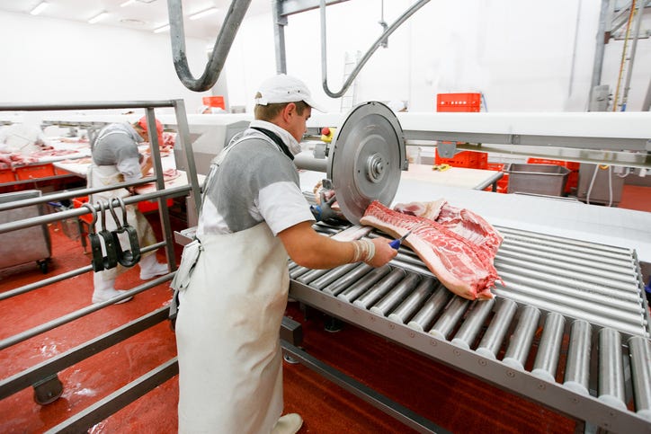 A group of workers in a meat factory, chopping fresh meat on work table.