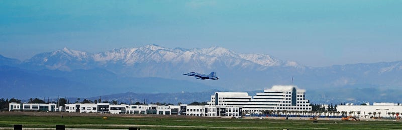 Fighter jet taking off from Long Beach Airport in Long Beach, CA. Snow covered mountains in the background.
