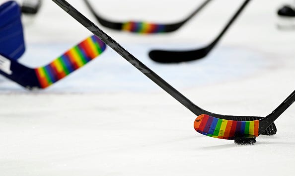 Hockey sticks during warm ups with pride tape.