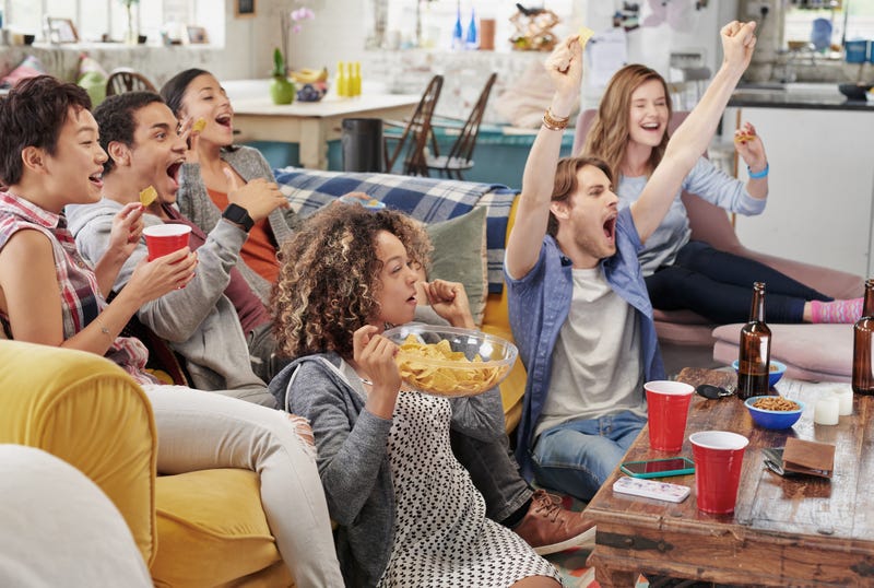 People gather around a couch to watch and cheer on a football game.