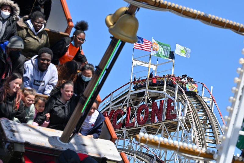 People riding the Cyclone are framed by people riding the ship ride at Luna Park on the opening day of the season at Coney Island on April 2, 2022 in Brooklyn.