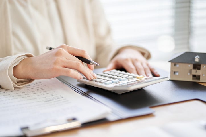 A woman's hands working on a calculator with a small toy model home nearby