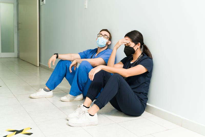 Exhausted nurse and doctor with face masks resting in the hospital aisle. Medical staff feeling tired