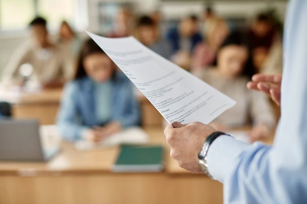 Professor lecturing students while holding a paper