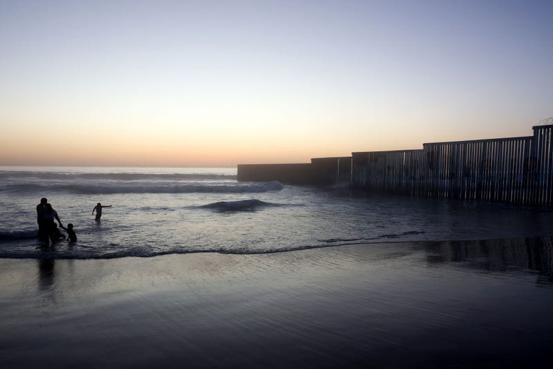 Beachgoers wade near the U.S.-Mexico border barrier which extends into the Pacific Ocean on April 7, 2022 in Tijuana, Mexico.