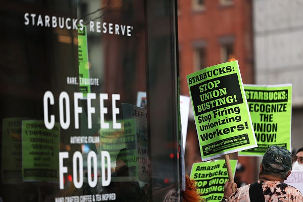 People hold signs while protesting in front of Starbucks on April 14, 2022 in New York City. Activists gathered to protest Starbucks' CEO Howard Schultz anti-unionization efforts and demand the reinstatement of workers fired for trying to unionize. 