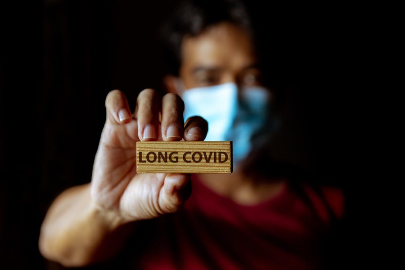 Masked  man show wooden sign with wording "Long Covid" in dark room.