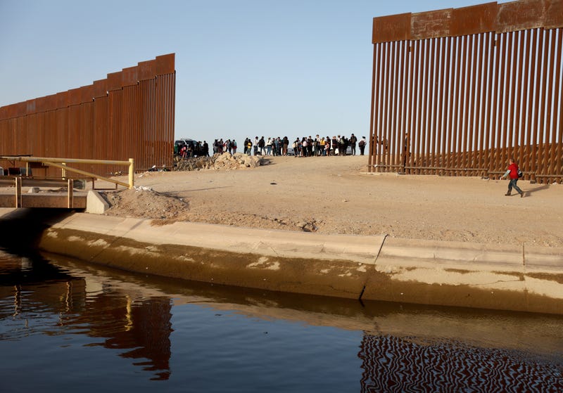 YUMA, ARIZONA- MAY 20: An immigrant (R) walks to cross through a gap in the U.S.-Mexico border barrier as others (C) await processing by the U.S. Border Patrol on May 20, 2022 in Yuma, Arizona. Title 42, the controversial pandemic-era border policy enacted by former President Trump, which cites COVID-19 as the reason to rapidly expel asylum seekers at the U.S. border, was set to officially expire on May 23rd. A federal judge in Louisiana delivered a ruling today blocking the Biden administration from lifting Title 42.