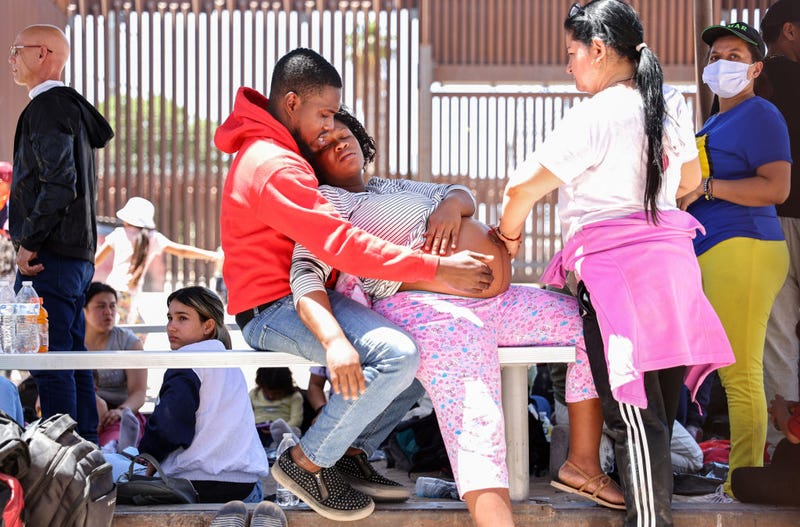 A pregnant immigrant from Haiti is assisted by her partner and another immigrant while having contractions, after she crossed from Mexico, with the U.S.-Mexico border barrier in the background, on May 21, 2022 in San Luis, Arizona. A U.S. Border Patrol agent soon opened a gate in the border barrier to allow paramedics to reach her, while was still technically in the United States. She had been stranded behind the barrier with other immigrants, some of whom said they had been waiting for two days to be picked up by Border Patrol. Title 42, the controversial pandemic-era border policy enacted by former President Trump, which cites COVID-19 as the reason to rapidly expel asylum seekers at the U.S. border, was set to officially expire on May 23rd. A federal judge in Louisiana delivered a ruling yesterday blocking the Biden administration from lifting Title 42. (Photo by Mario Tama/Getty Images)