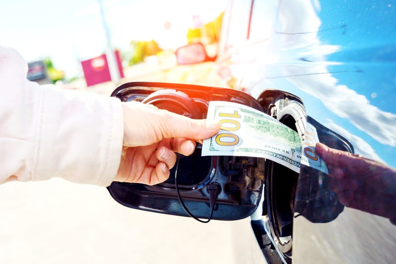 Person putting $100 bill into their gas tank.