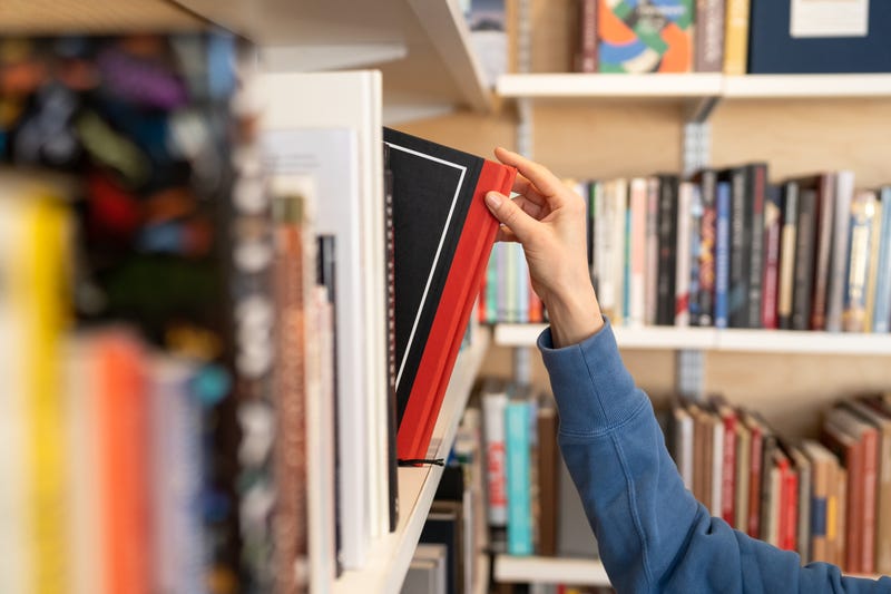 person grabbing a book from a library book shelf