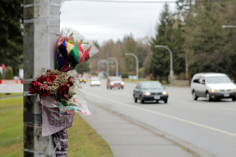 flowers taped up on a street light on the side of a busy road indicating someone's death 