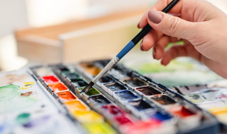Hand of artist holding paintbrush and choosing color of watercolor