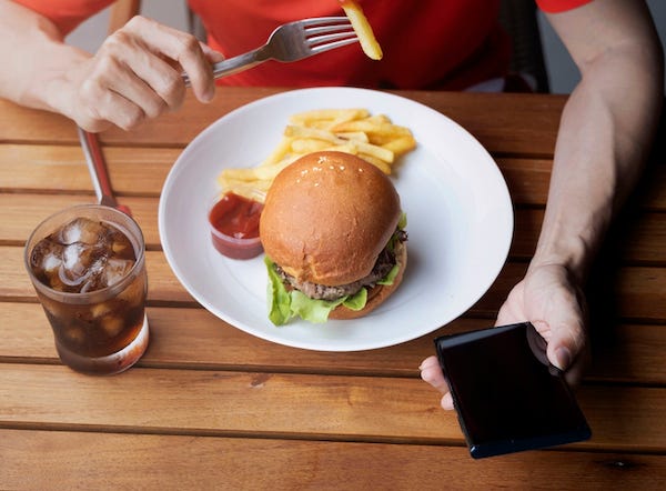 Man using smartphone while eating a hamburger