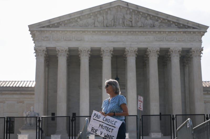A woman stands in front of the Supreme Court with a sign that reads "Pro choice, protect Roe v. Wade."