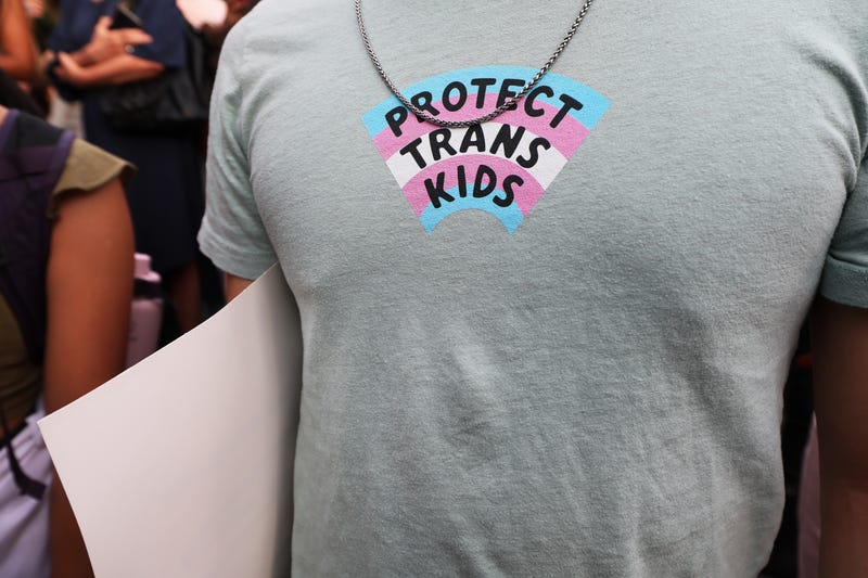 close up of shirt that says protect trans kids over a trans flag