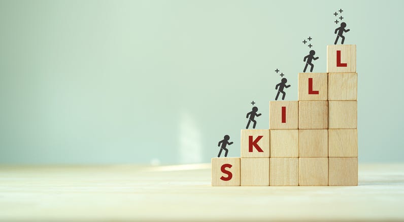 Concept of people climbing wooden blocks that spell out "skills"