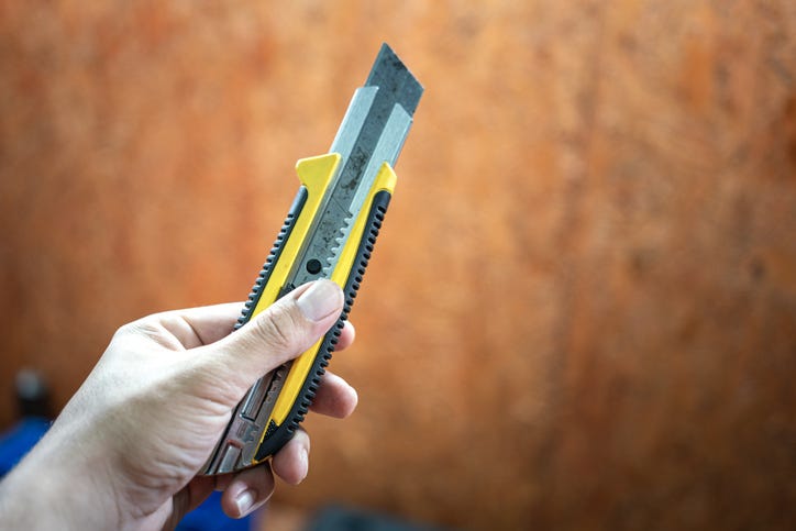 A left hand is holding a box cutter