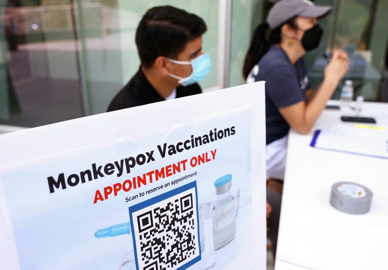 workers behind a table with a sign that says monkeypox vaccinations appointment only